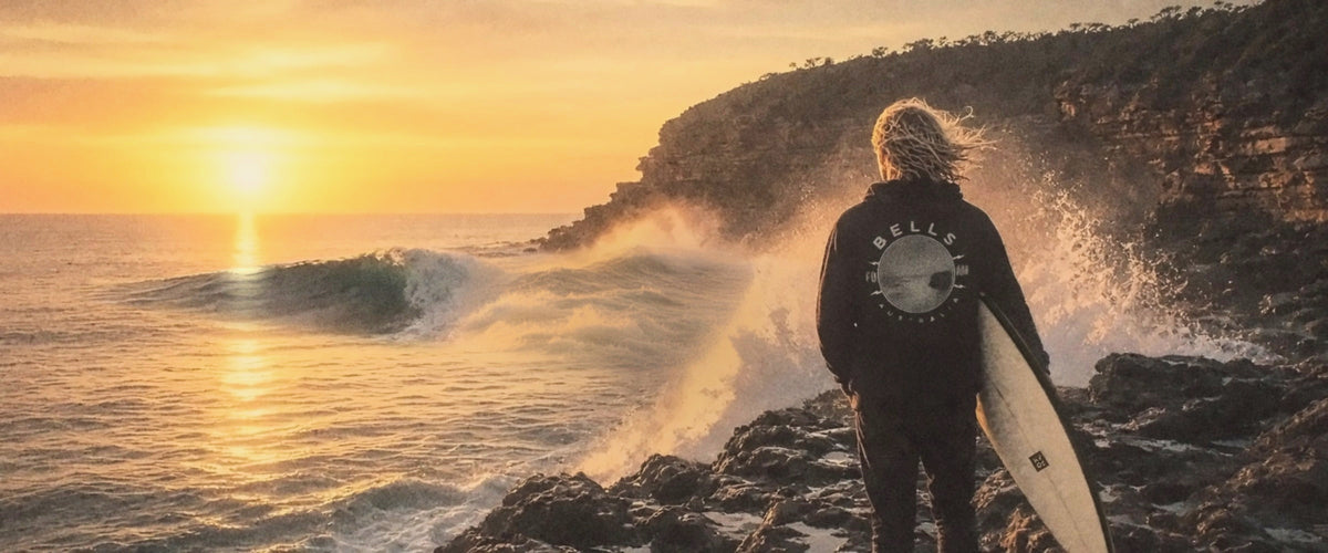 Surfer in a Foam Riders Bells hoodie watching waves at sunset